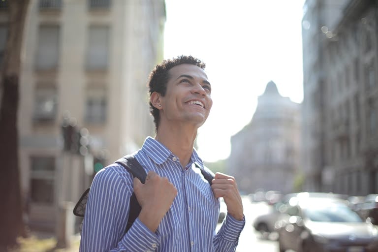 A joyful young man in a striped shirt enjoys a sunny day in the city, radiating happiness.