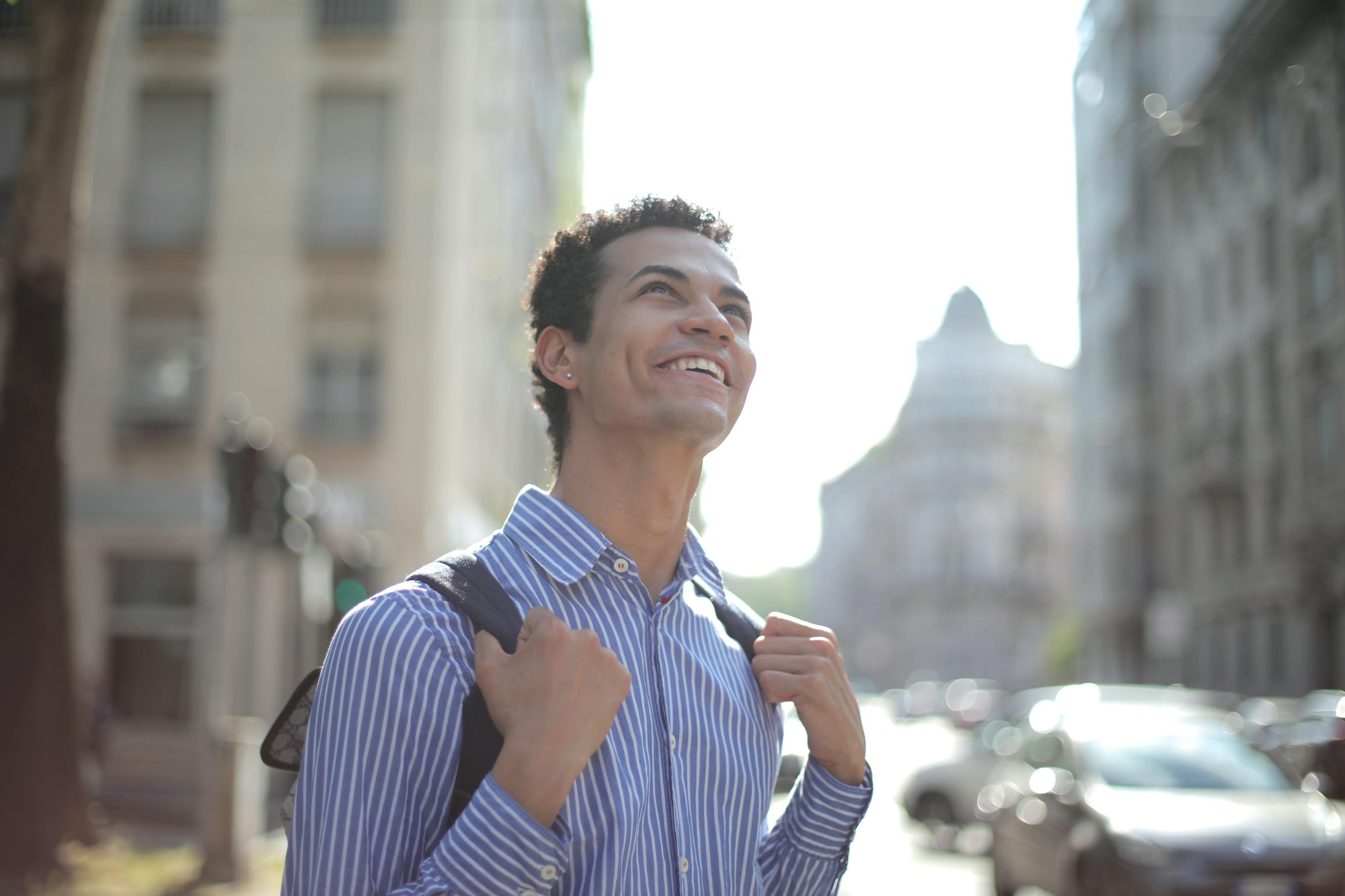 A joyful young man in a striped shirt enjoys a sunny day in the city, radiating happiness.