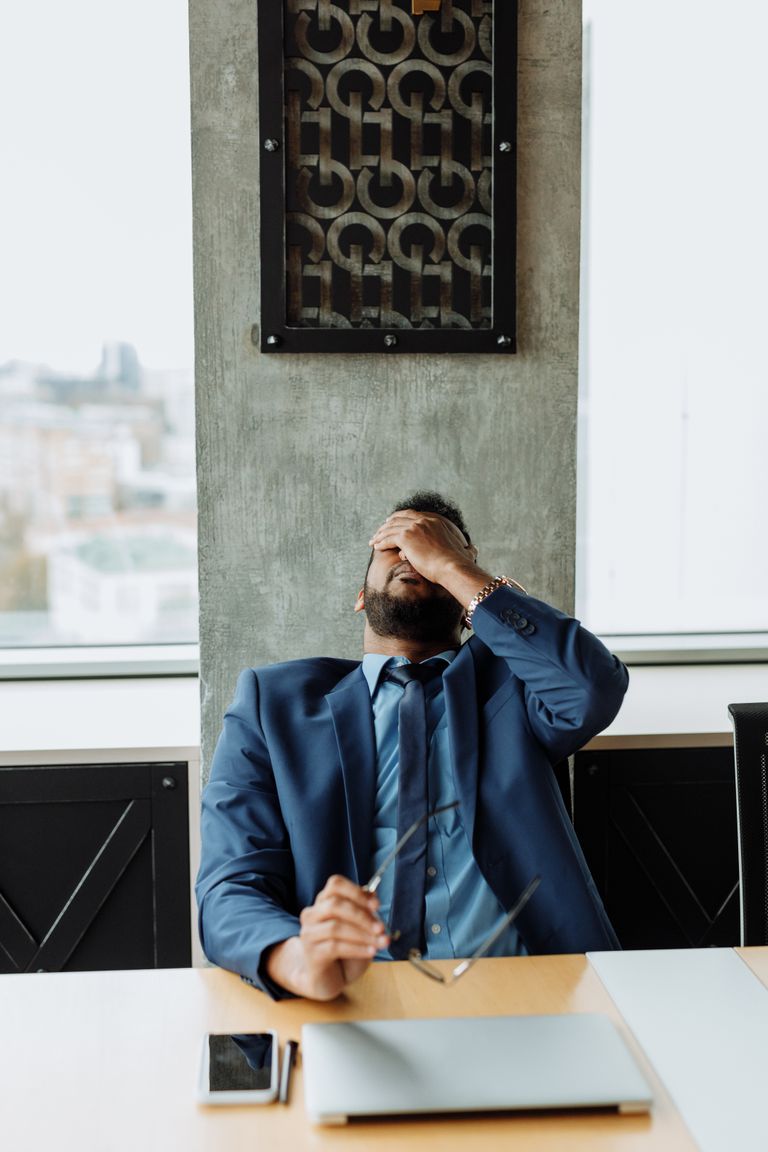 Overwhelmed businessman feeling stressed at work, holding head in hands.