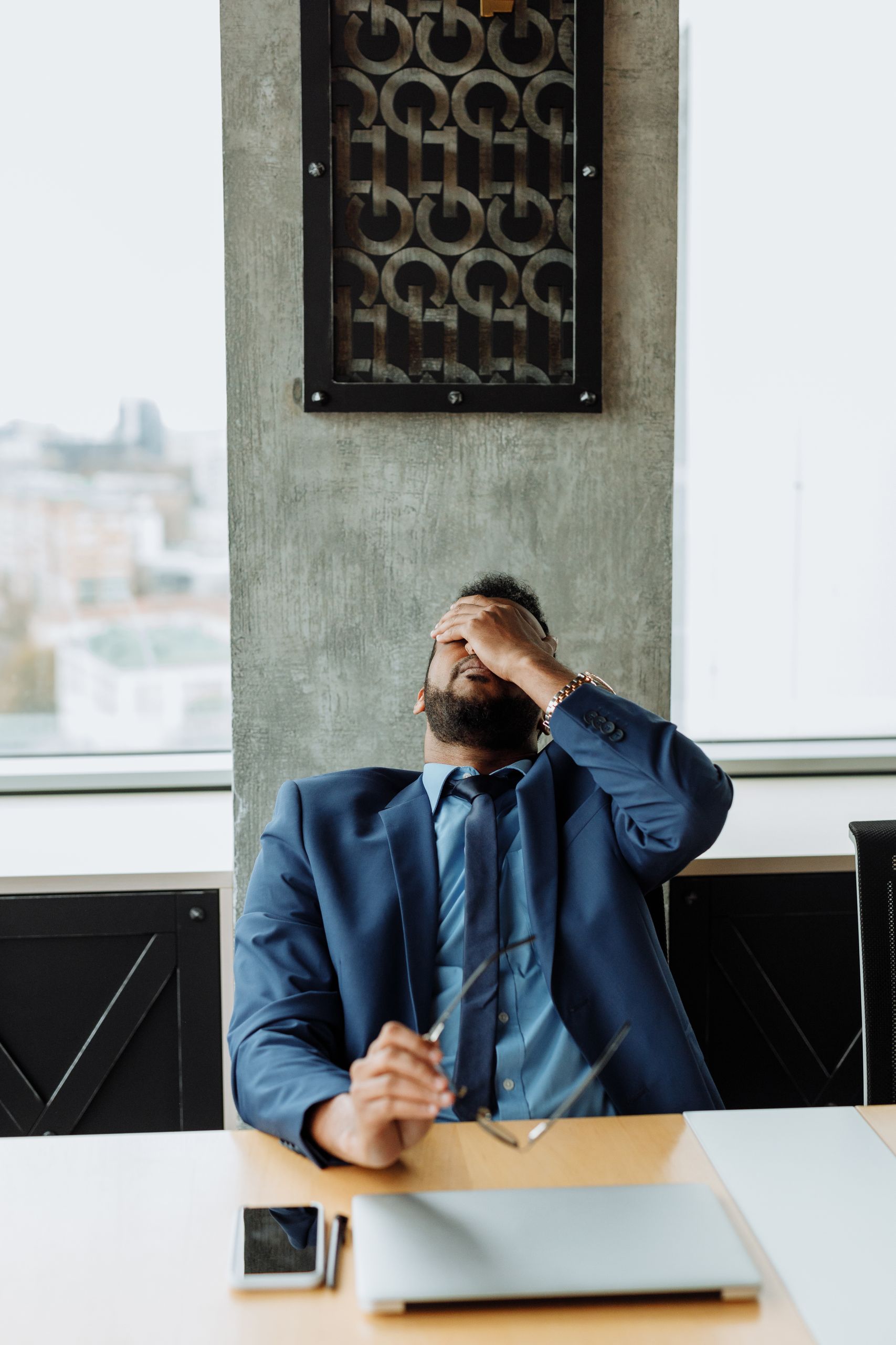 Overwhelmed businessman feeling stressed at work, holding head in hands.