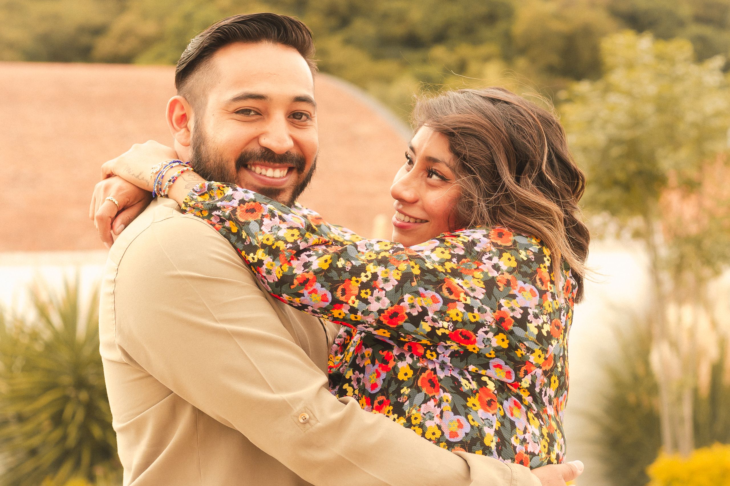 Smiling couple embracing outdoors in a warm, sunny setting. Vibrant and joyful atmosphere.