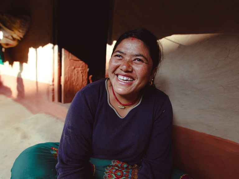 Smiling woman in traditional attire seated indoors, basking in natural light, exuding joy and warmth.